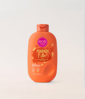 A bottle of EOS Pumpkin Chai body lotion on a light gray background. The bottle is bright orange with a matching flip-top cap, featuring a label with a pink EOS logo and autumn-themed graphics.