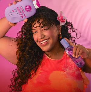 A smiling woman with long curly hair holds two purple bottles from the brand e.l.