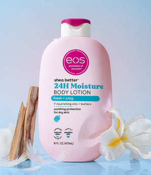 Pink bottle of eos 24H Moisture Body Lotion on a light blue background with flowers and wooden elements.