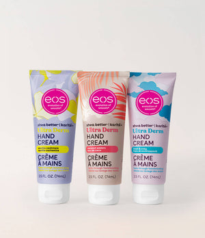 Three EOS brand hand cream tubes standing upright on a light neutral background. The left tube is lavender with yellow accents, the middle tube is beige with coral accents, and the right tube is light purple with blue accents.