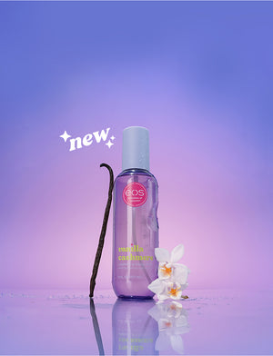 Bottle of EOS Vanilla Cashmere body mist with a vanilla bean and orchid flower on a purple background