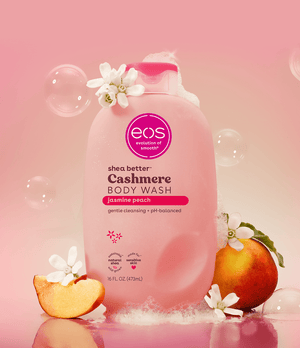 Pink bottle of eos Cashmere Body Wash with jasmine peach scent on a pink background with peaches and flowers.