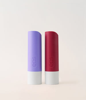 Two eos lip balm tubes, one purple and one red, on a light beige background.